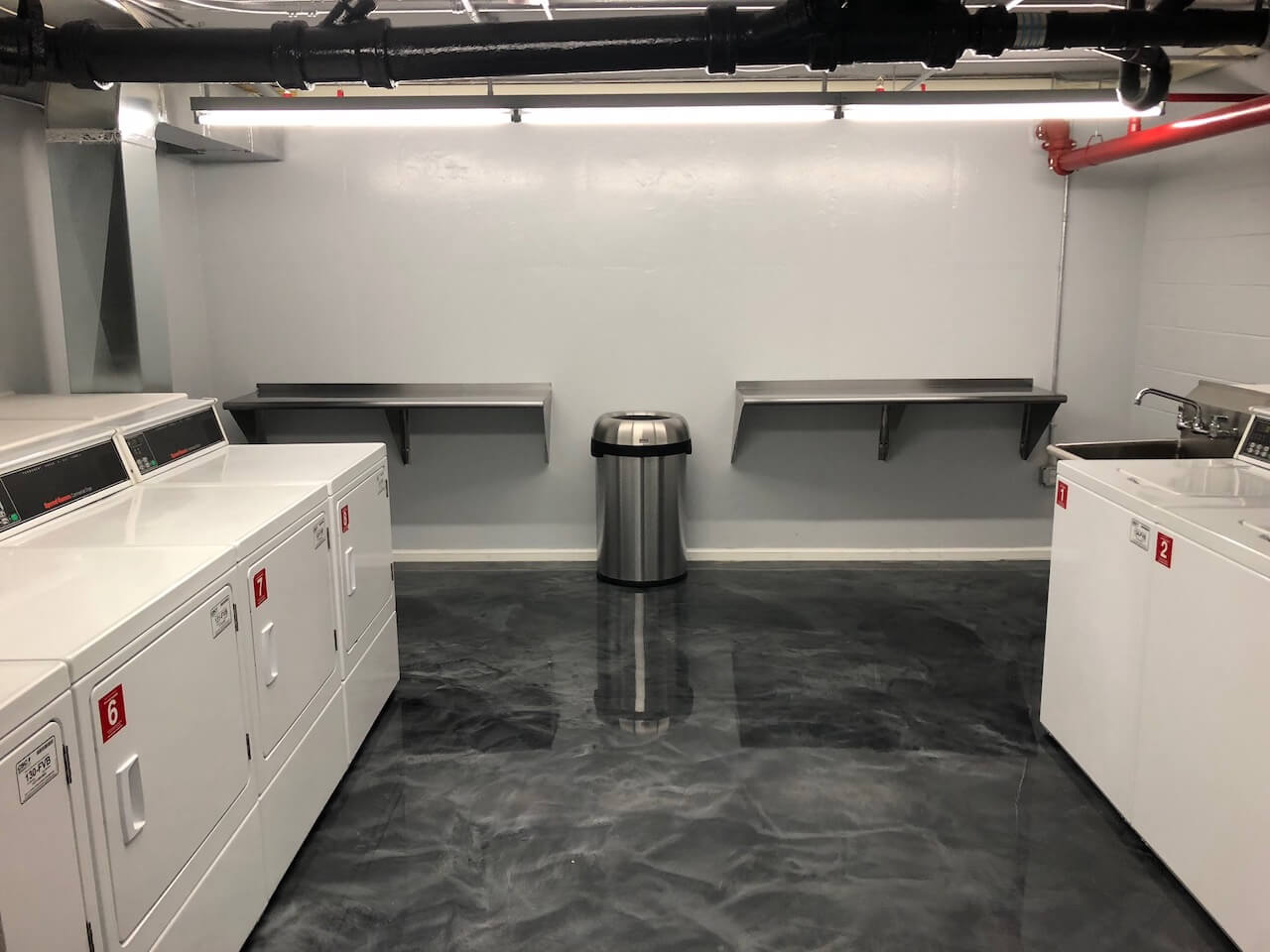 A dark gray and black epoxy floor installed in the basement laundry room of a multi-family property.