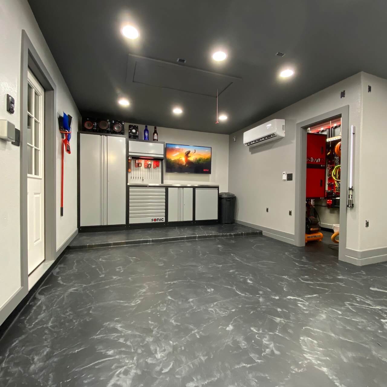 This metallic epoxy garage floor features a dark gray base with white highlights.  The garage has been completely remodeled and even has a TV and an air conditioner