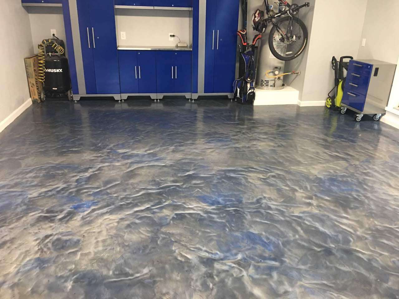 A truly unique epoxy garage floor.  The colors on this floor are blended in such a way as to create a wave-like design.  The garage also features premium blue garage cabinets.