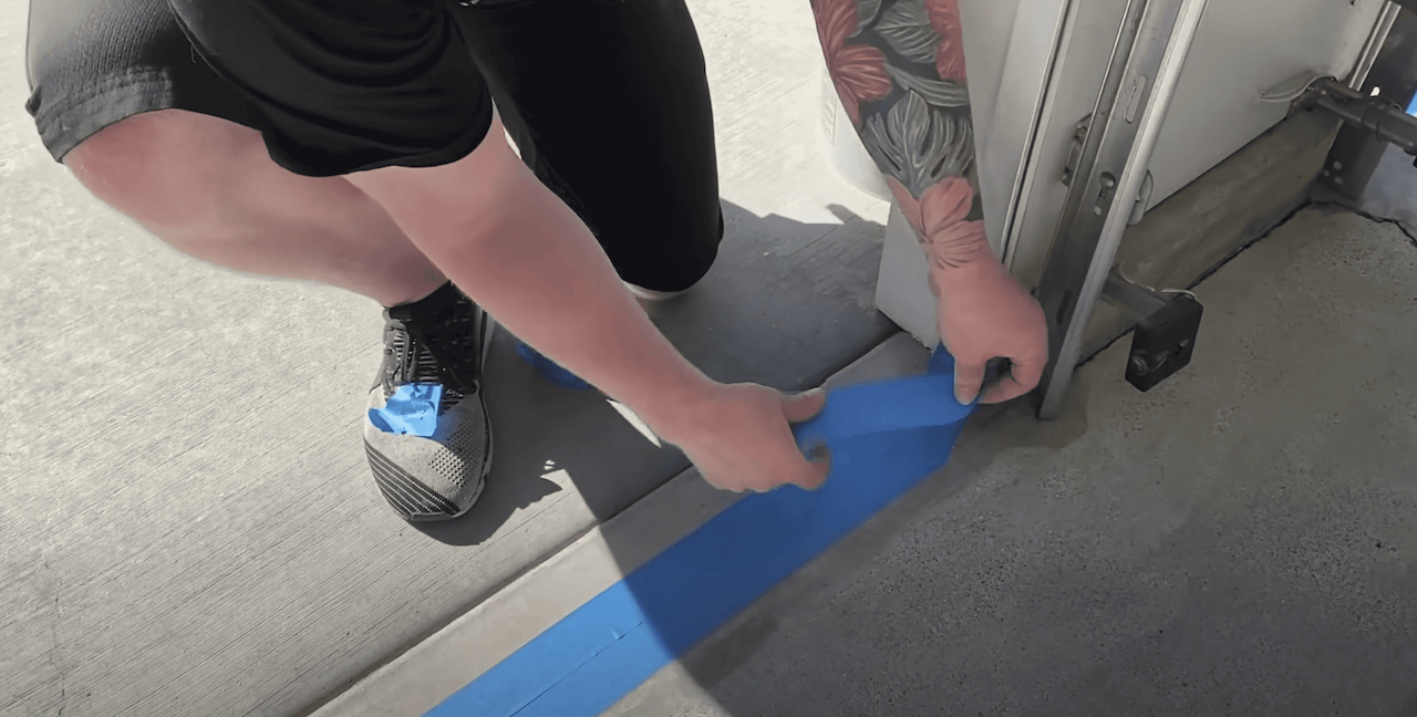 Placing blue painters tape at the edge of the garage door to create a perfect edge between our new hardwood overlay and the existing concrete outside.