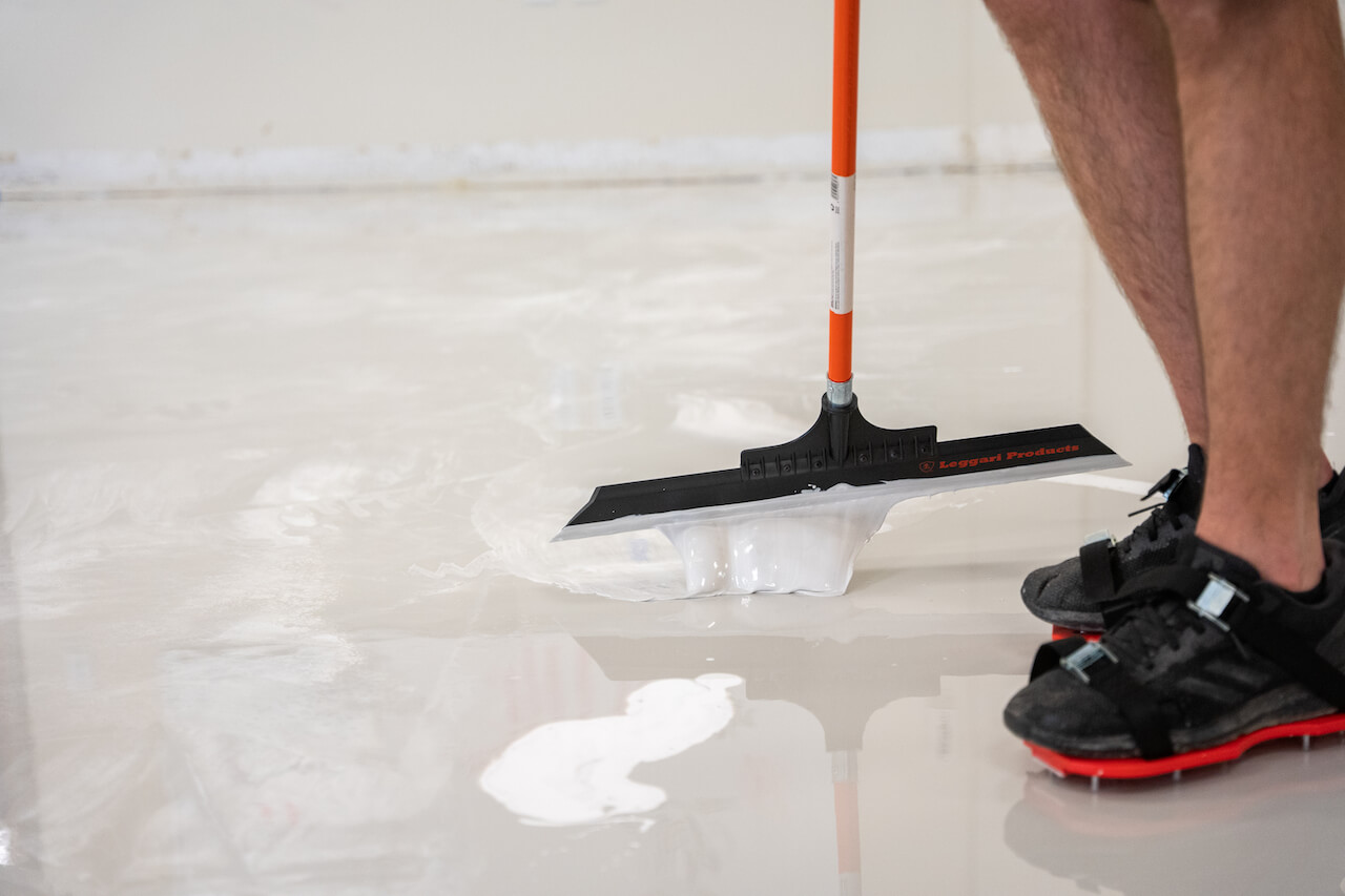 Spreading white epoxy on new floor using a Leggari squeegee while wearing spike shoes