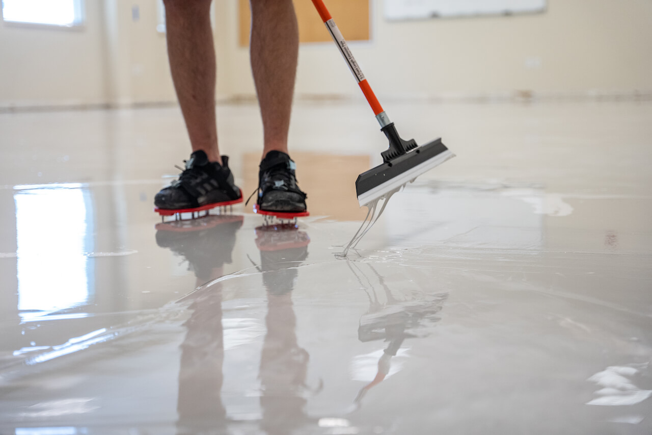 Using a leggari squeegee to apply epoxy on a large concrete floor.  The installer is wearing Leggari spike shoes.